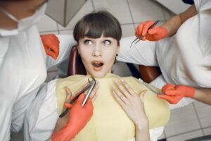 A female patient looking surprised while being examined by dentists in a clinic.